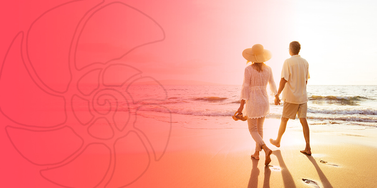 A woman in a sun hat and a man holding hands while walking on the beach.